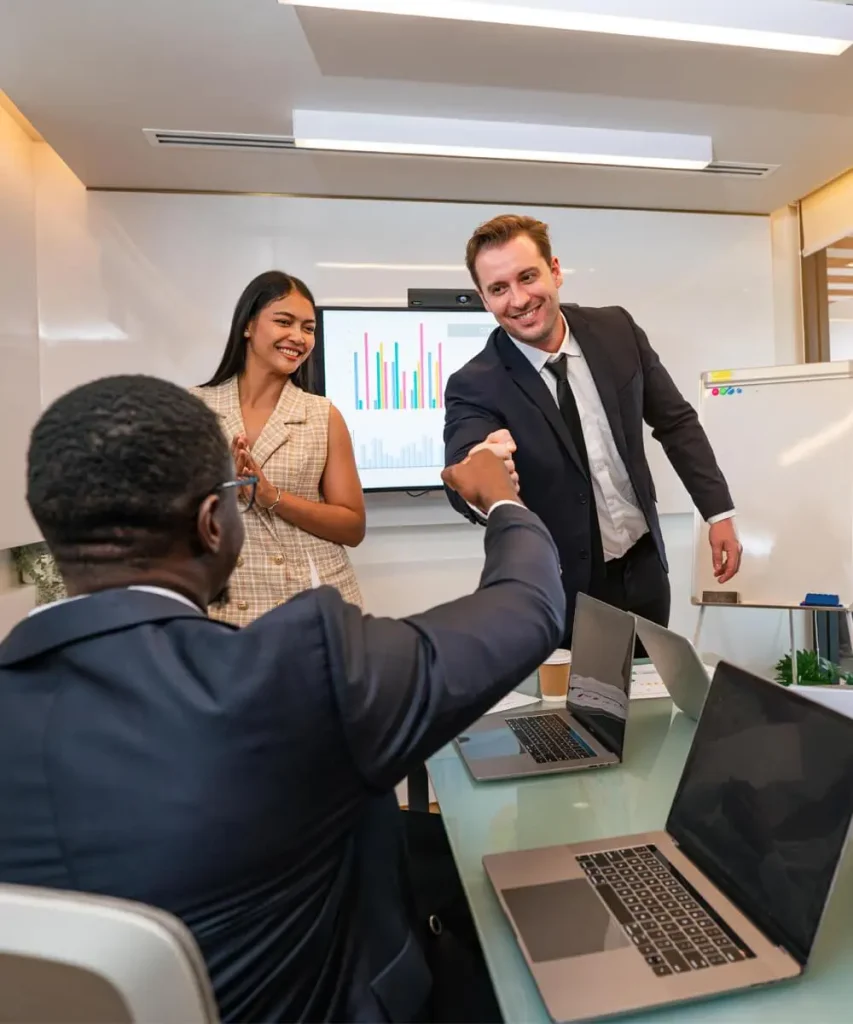 Two men fist bumping out of excitement while a woman smiles at them in an office setting.